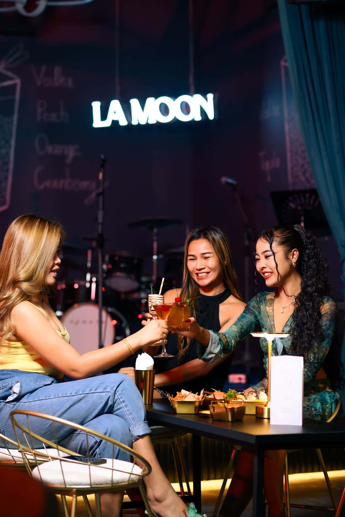 Four guests raising glasses at a table under the neon La Moon sign