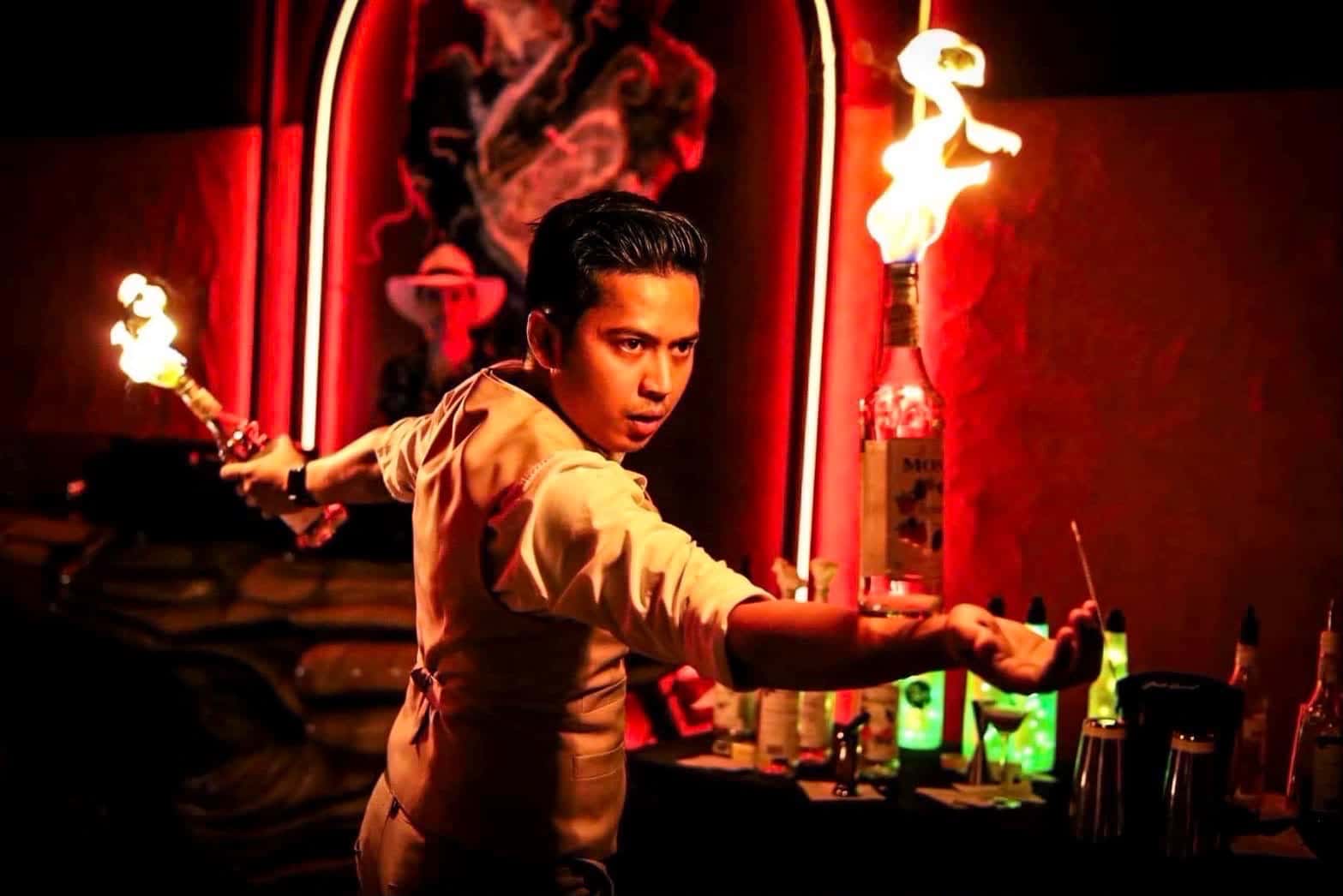 Patiwat Rotoiu, the flair bartender at La Moon, holding two lit torches behind the bar
