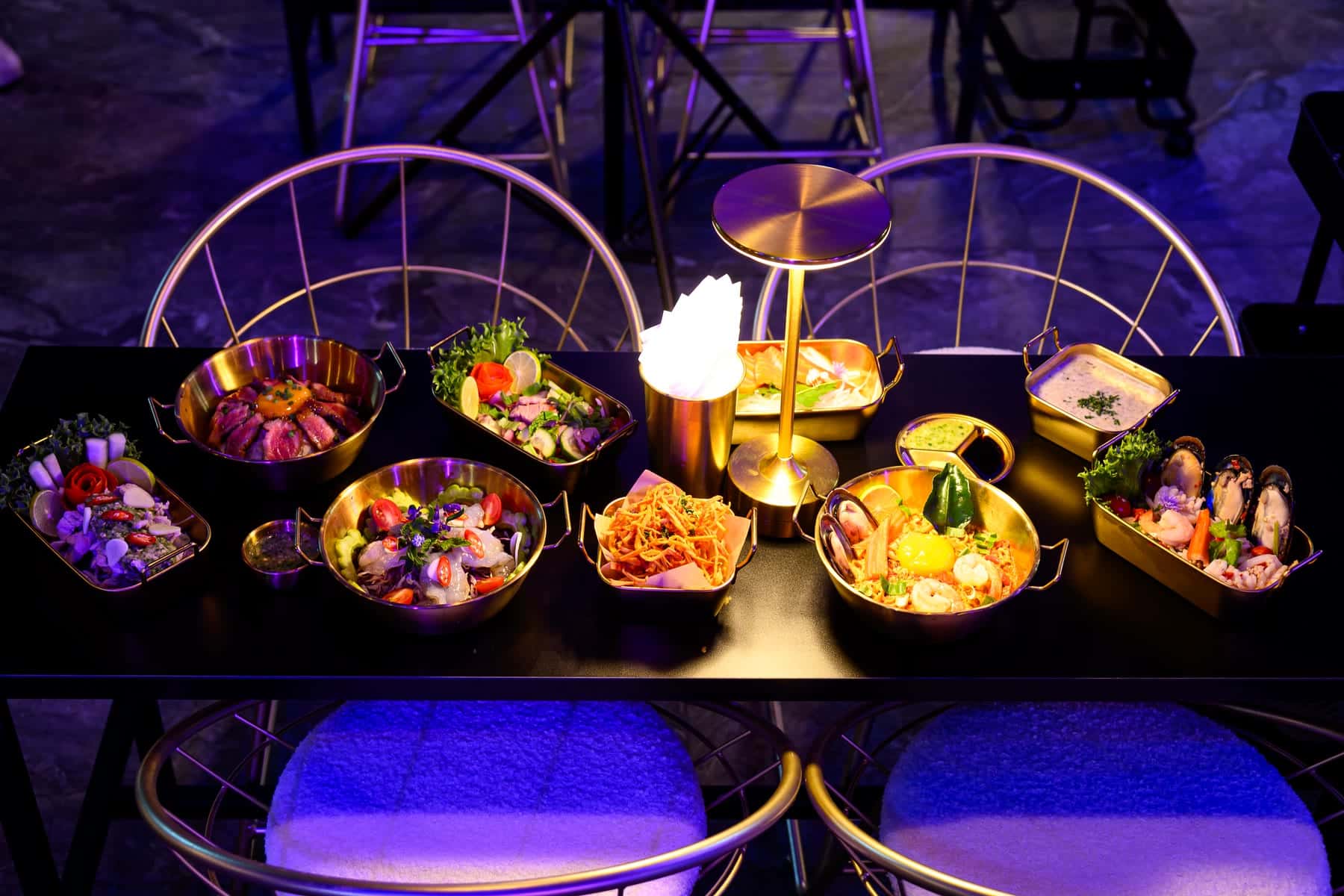 A spread of gold serving dishes on a dark table at La Moon