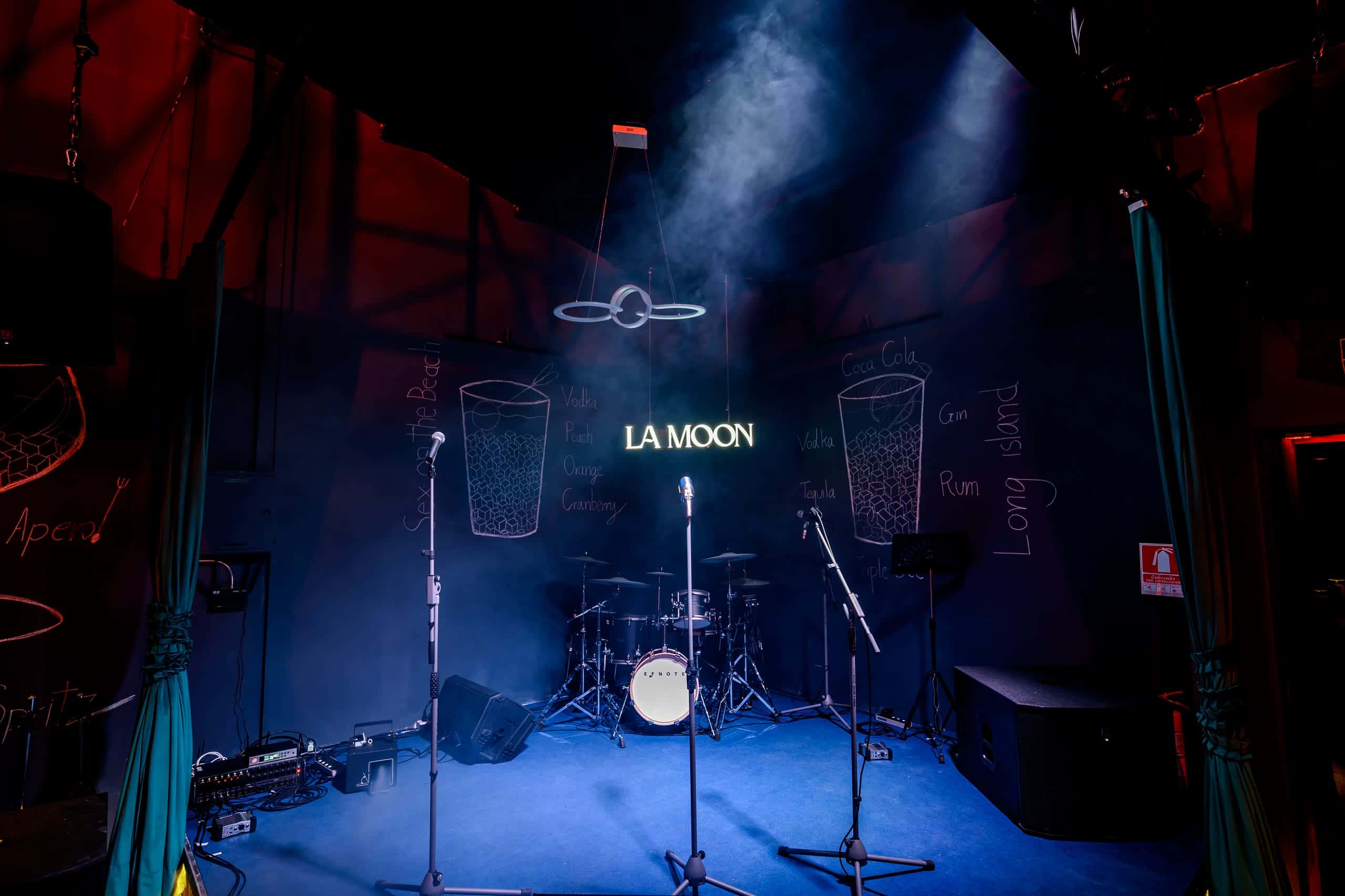 The empty stage at La Moon, lit blue, with the neon sign behind the drum kit