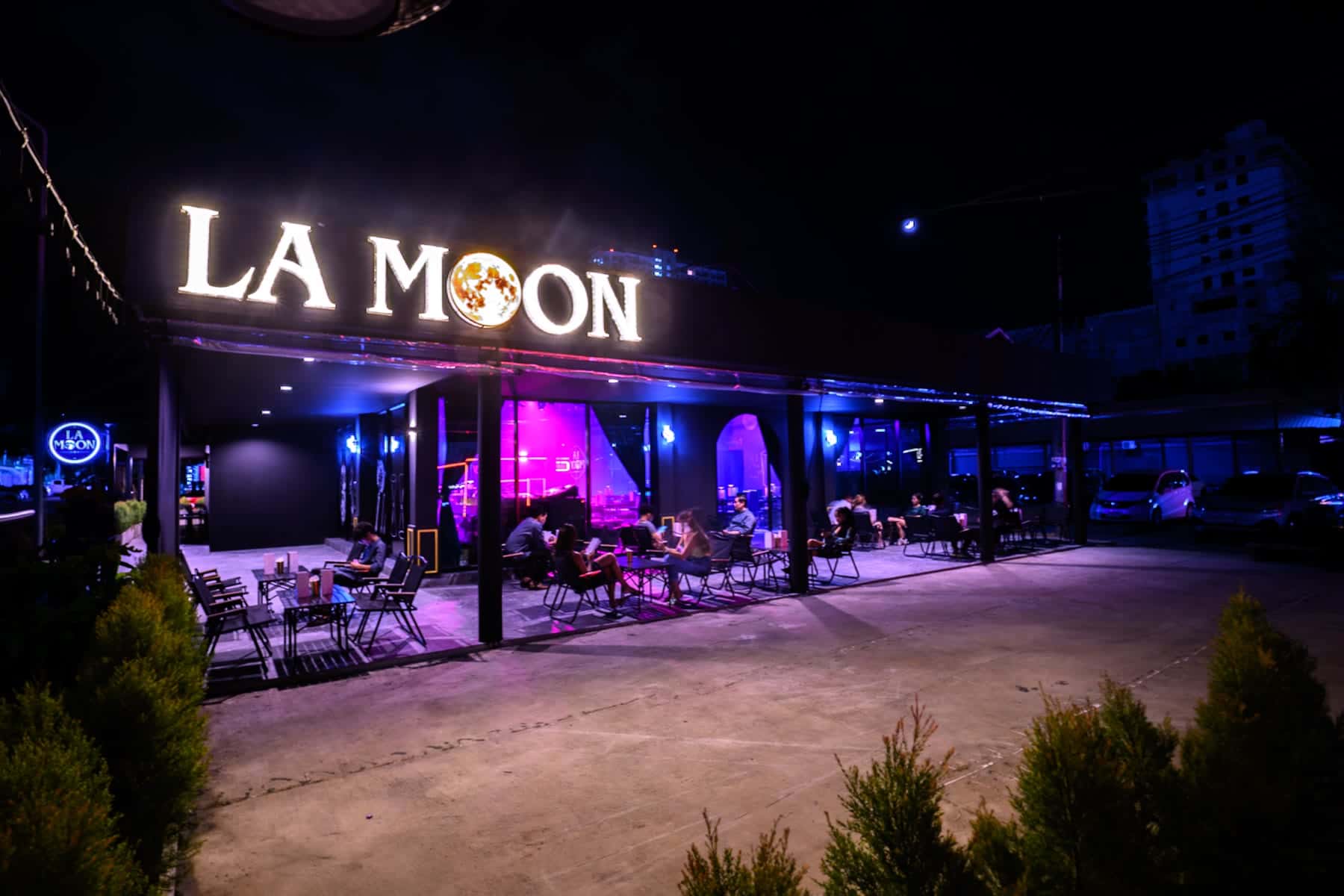 The lit La Moon sign above the entrance, seen from the forecourt at night