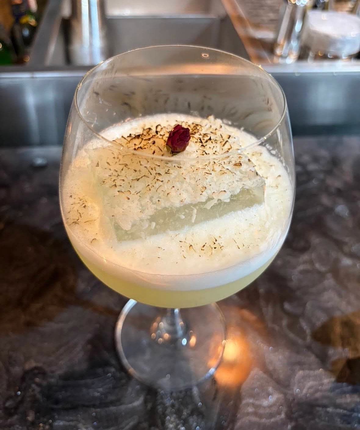 A coupe glass of pale foam dusted with grated nutmeg, a single berry on top
