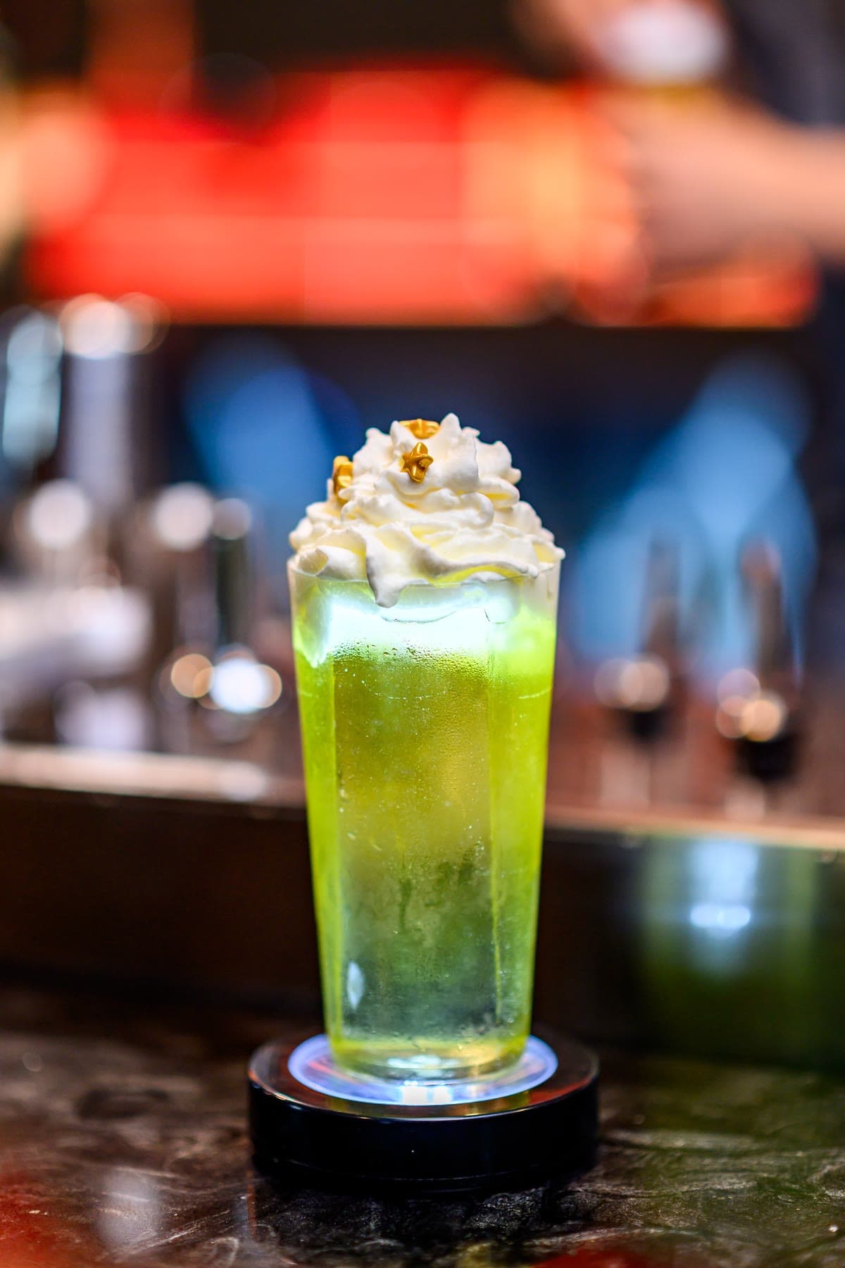 A tall bright green cocktail under a cap of whipped cream finished with gold leaf