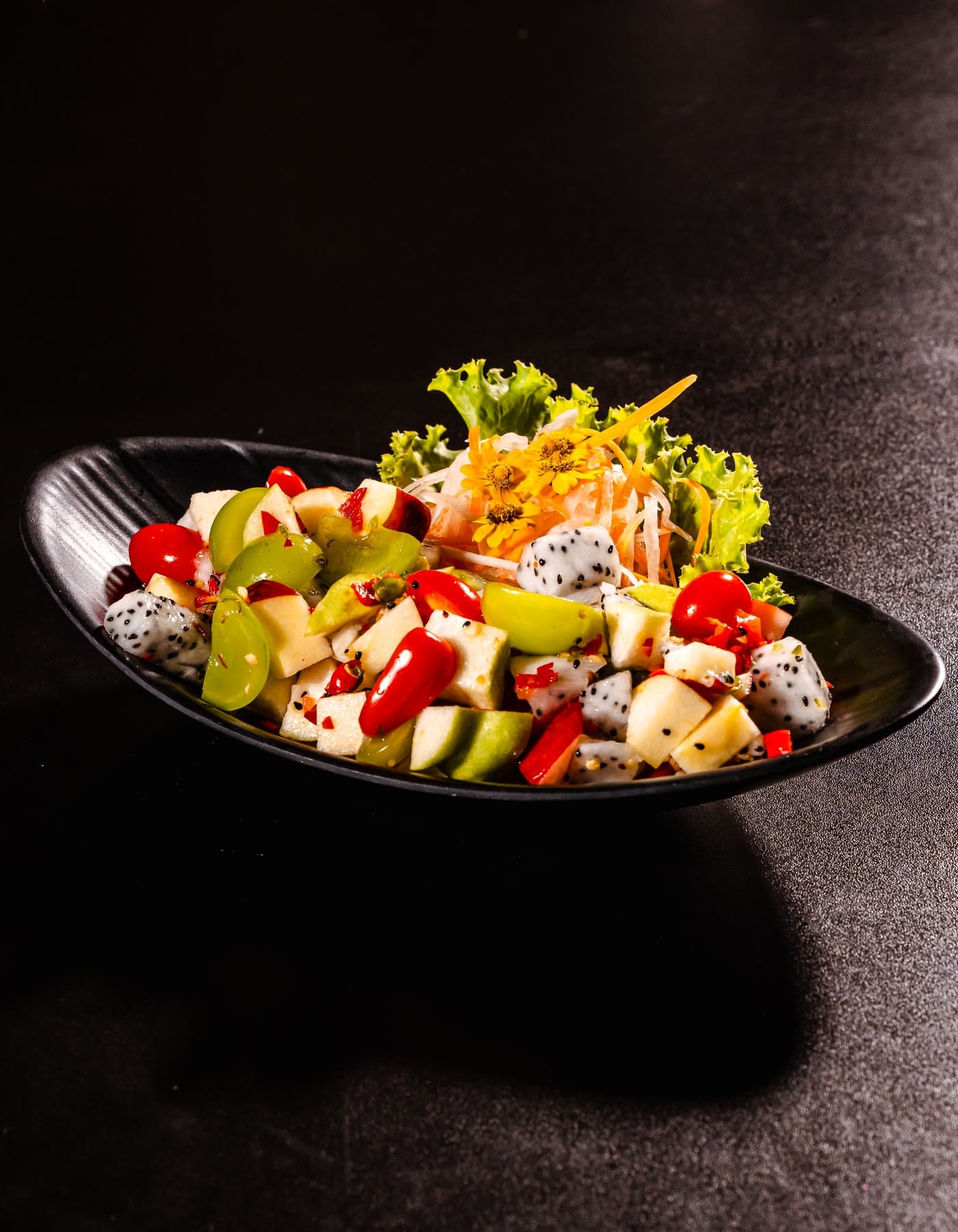 Cole' Lamoon fruit salad: dragon fruit, apple and grapes with a carved carrot rose on a black plate