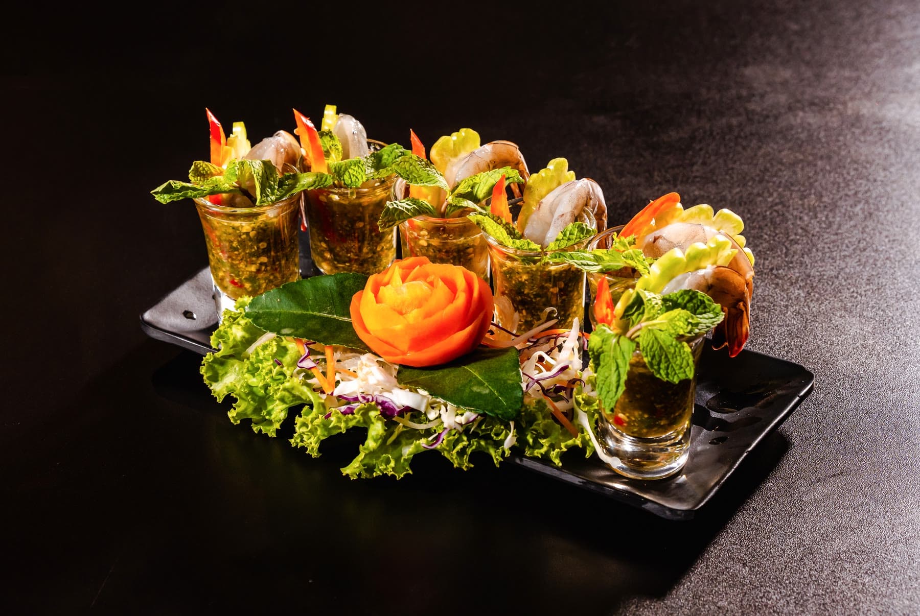 Shrimp shots: prawns served upright in small glasses on lettuce with a carved carrot rose