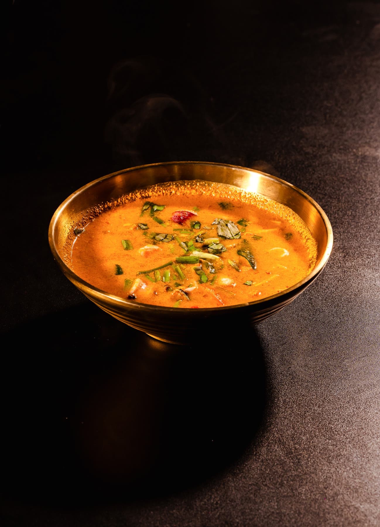 Seafood tom yum in a gold bowl, red broth with herbs and prawns