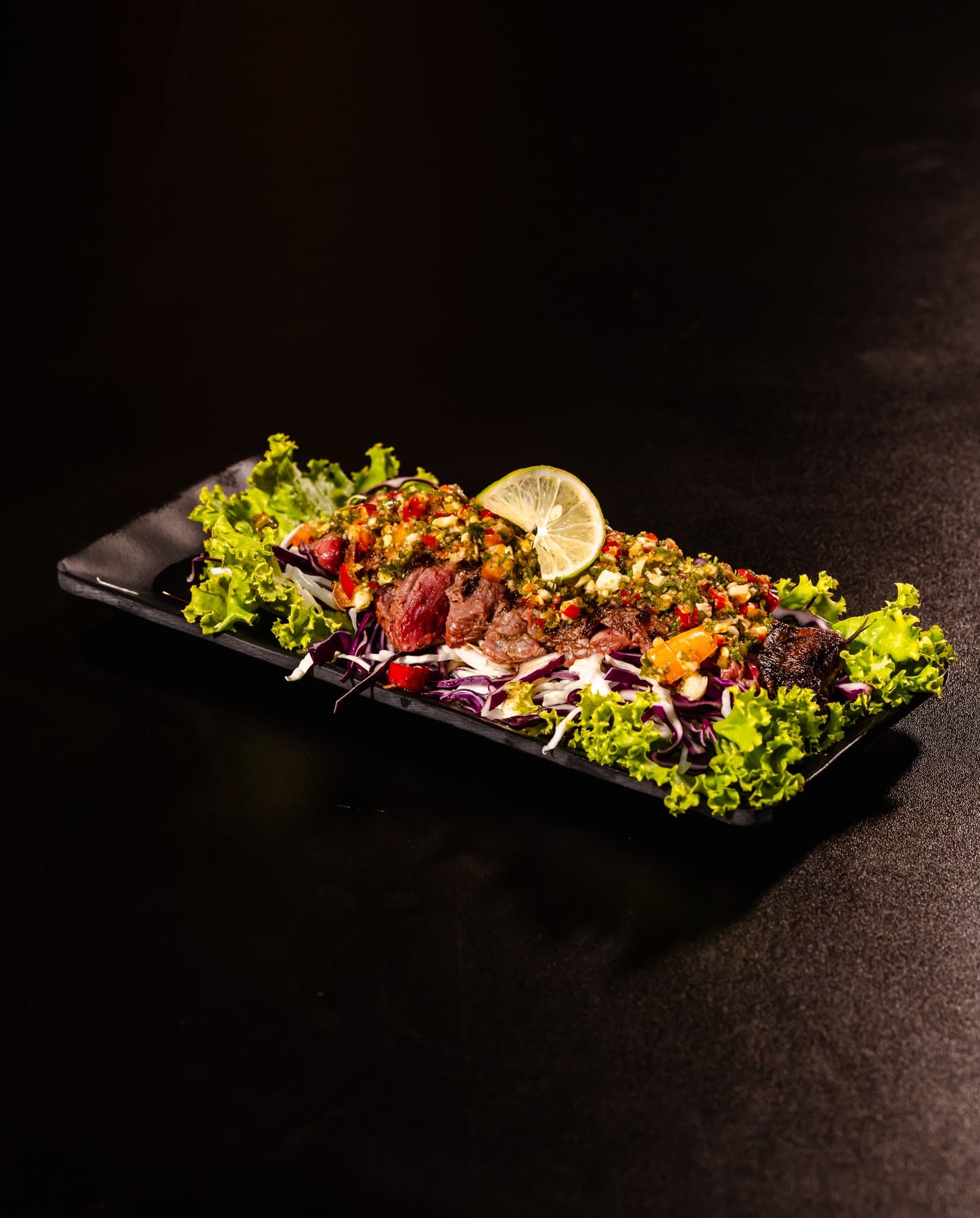 Spicy wagyu beef salad, sliced beef with herbs and lime on a long black plate