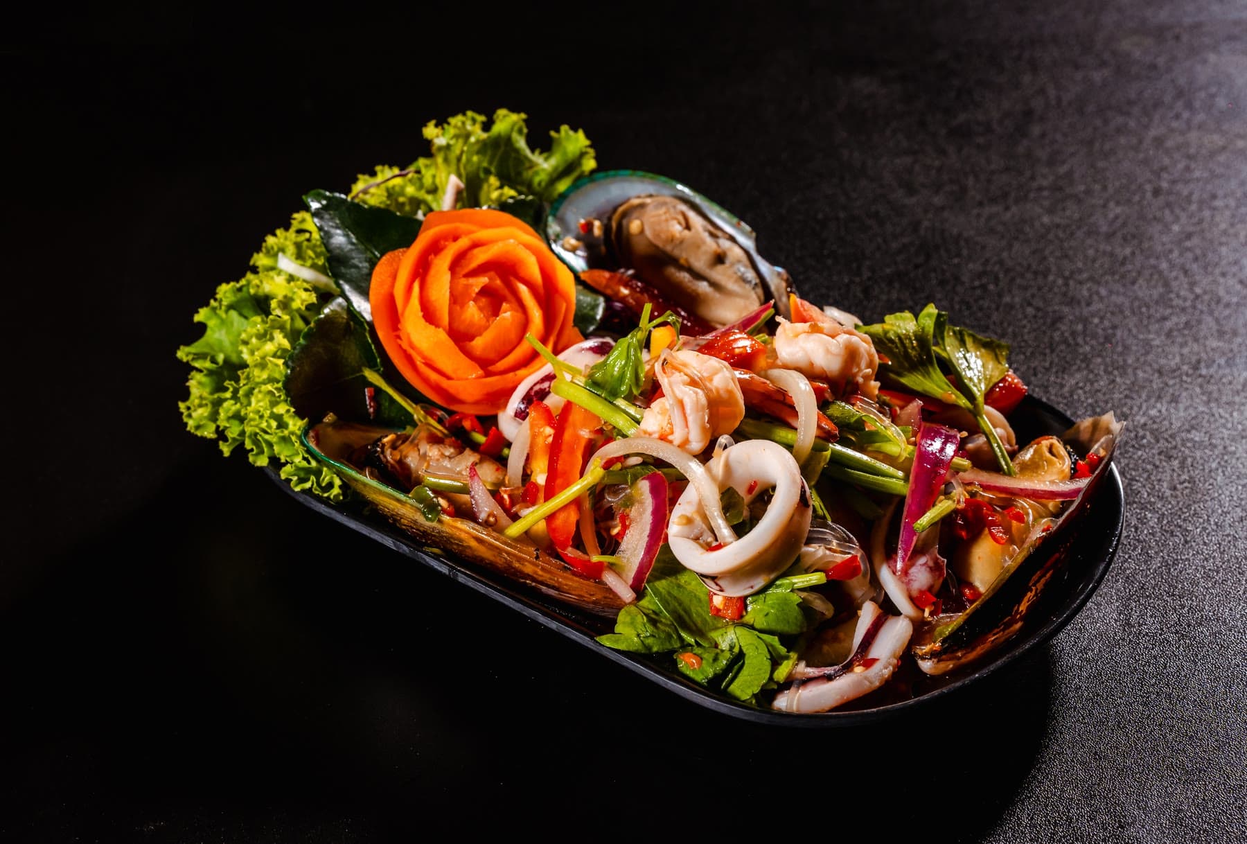 Spicy seafood salad with squid, mussels and red onion on a black plate